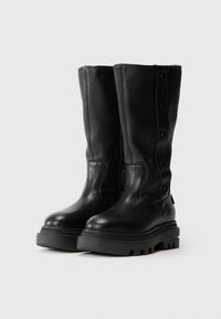 Botas de cuero negras hasta la rodilla con un acabado texturizado, punta redonda, suela de goma negra gruesa y detalles de botones en el lateral.