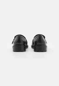 Zapatos de cuero negro con un acabado suave, punta redondeada y una suela de goma baja y estriada. Presentan una correa en el talón para mayor estabilidad.