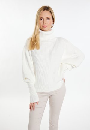 Pulover alb cu guler înalt și textură ribată, cu mâneci largi și o croială lejeră, combinat cu pantaloni bej deschis, pe un fundal simplu.