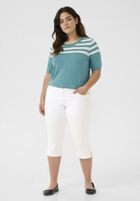 Top de punto en color verde azulado con rayas horizontales blancas, combinado con pantalones capri blancos. Los pantalones tienen aberturas laterales en el dobladillo. Unos zapatos planos negros completan el conjunto.
