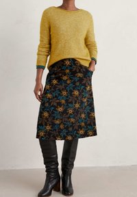 Żółty, miękki sweter dziany z prążkowanymi mankietami, zestawiony z czarną spódnicą w kwiaty w kolorze brązowym i niebieskim, noszony z czarnymi kozakami do kolan.