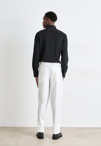Black long-sleeve shirt with a ribbed collar, paired with white trousers featuring a relaxed fit and elastic waistband. Black shoes complete the look.