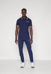 Marine polo shirt med kontrasterende hvid krave og ærmetrim, parret med matchende marine sportbukser og hvide sneakers.
