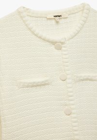 Cárdigan color crema con un tejido texturizado, cuello acanalado y dos bolsillos frontales. Abrochado con botones redondos de color claro.