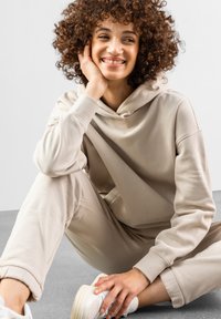 Beige hoodie og matchende sweats med blødt stof. Hoodien har en behagelig snor og en afslappet pasform. Hvide sneakers.