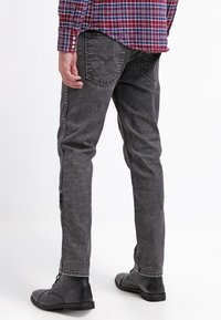 Vyprané černé džíny s úzkým střihem, vybavené dvěma zadními kapsami a jemnou texturou. Nošeny s černými šněrovacími botami a kostkovanou košilí.