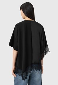 Sort top med et tekstureret blondekant, featuring en afslappet pasform og korte ærmer, lavet af et glat, let materiale.