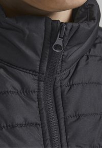 Close-up of a black quilted jacket collar with a centered zipper partially zipped near a person's neck.