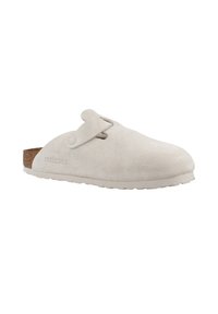 Chaussure slip-on en daim blanc avec un bout arrondi, semelle en liège, sangle réglable et semelle en caoutchouc. Design minimaliste sans motifs visibles.