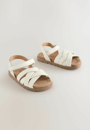 Sandales blanches avec un design tressé, fabriquées en matériau synthétique, dotées d'une semelle en liège et d'une bride de cheville ajustable.