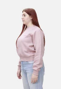 Felpa rosa con polsini e orlo a costine, caratterizzata da collo rotondo e ricamo con logo. Abbinata a jeans azzurri.