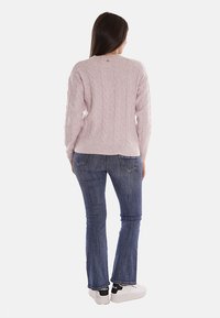 Pullover rosa lavorato a maglia con motivo a treccia, maniche lunghe e orlo a costine. Abbinato a jeans a zampa d'elefante blu e sneaker bianche.