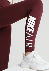 Vinröda leggings med "NIKE AIR" i fet vit text längs sidan, kombinerat med en vit sportskor med en framträdande logotyp.