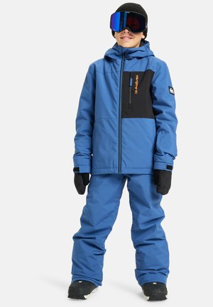 Veste de ski bleue avec accents noirs, poches zippées et logo. Associée à un pantalon de ski bleu assorti et des gants noirs, le tout étant imperméable.