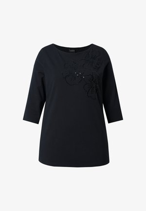 Zwart katoenen t-shirt met driekwart mouwen, voorzien van een bloemmotief van zwarte pailletten aan de voorkant. Eenvoudige ronde halslijn.