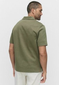 Lyhythihainen, tummanvihreä poolopaita teksturoitua kangasta, jossa on kauluskoneisto, suora leikkaus ja sivuhalkiot helmassa.