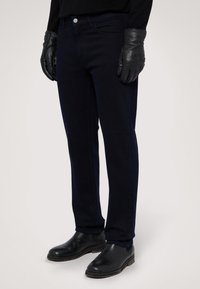 Jeans azul marino de denim, con un ajuste entallado, bolsillos frontales, cierre de botón metálico, y combinados con guantes y botas de piel negra.