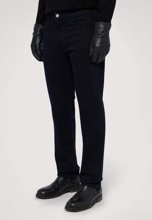 Jeans bleu marine en denim, avec une coupe slim, des poches avant, une fermeture à bouton en métal, associés à des gants en cuir noir et des bottes.