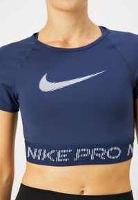 Top corto atlético de manga corta en azul marina con el logo blanco de Nike y el texto "NIKE PRO" en la cinturilla elástica. Diseño suave y ajustado.