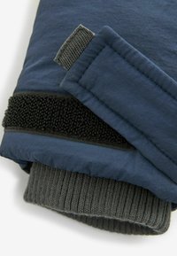 Marineblaues gestepptes Gewebe mit einem strukturierten schwarzen Klettverschlussriemen und einem grauen gerippten Strickbund am unteren Ende. Mehrere sichtbare Schichten.