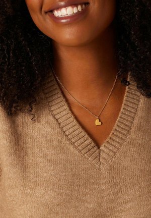 Goldener Herzanhänger an einer zarten Kette, kombiniert mit einem beigen, gerippten Pullover mit V-Ausschnitt.