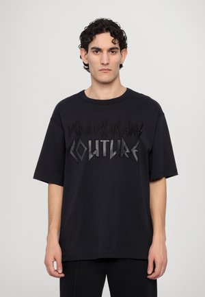 Black short-sleeve t-shirt featuring raised textured logo reading "VERSACE JEANS COUTURE" in bold, angular lettering across the front.