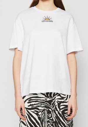 Hvid t-shirt med en lille gul sol og teksten "LIFE IS GOOD" over brystet, kombineret med sort-hvide zebramønstrede bukser.