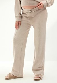Beige weit geschnittene Sweatpants aus einem weichen, strukturierten Stoff mit einem Kordelzugbund und sichtbaren Seitennähten.