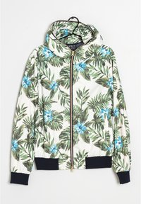 Witte ritsjack met capuchon, versierd met een patroon van groene tropische bladeren en blauwe bloemen, zwarte manchetten en een tailleband, hangend aan een hanger.