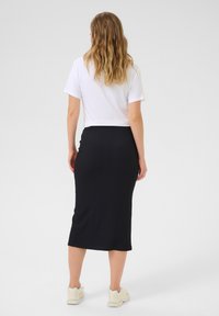 Jupe midi noire à côtes avec une silhouette ajustée, associée à un haut blanc à manches courtes et des baskets de couleur claire, vue de l'arrière.