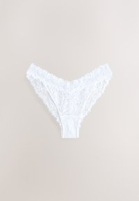 String en dentelle blanche avec motifs floraux et bords festonnés, posé à plat sur un fond beige.