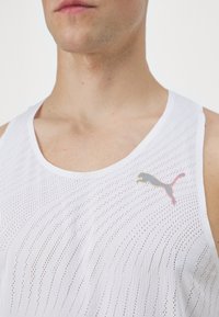 Canottiera bianca senza maniche realizzata in un tessuto a rete traspirante, con un logo Puma grigio e rosa sulla parte sinistra del petto.