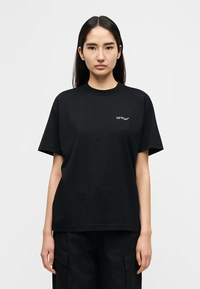 Μαύρο βαμβακερό t-shirt με άνετη εφαρμογή, που διαθέτει μικρό πράσινο λογότυπο στην αριστερή πλευρά του στήθους και κοντά μανίκια. Απλός σχεδιασμός, χωρίς μοτίβα.