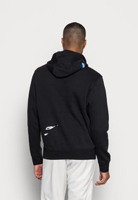 Svart hoodie i bomullsblandning. Har en framficka i kengurustil, ribbade ärmar och en blå accentlogotyp på huvan. Vit logotyp på baksidan.