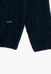 Maglione a coste di colore blu navy con polsini a coste, dotato di una piccola etichetta con logo. Il tessuto presenta un aspetto morbido e testurizzato.