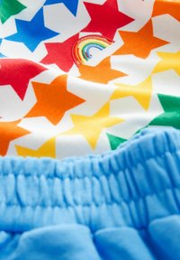 Tela con un patrón de estrellas multicolores y un pequeño arcoíris bordado, combinada con una suave cinturilla elástica azul.