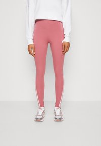 Leggings cor-de-rosa com riscas brancas nas laterais, feitas de um material elástico. Combinados com uma parte superior de manga longa branca e tênis de corrida cinzas.
