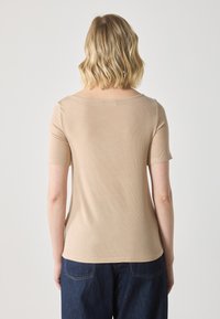 Haut beige à manches courtes avec une texture côtelée douce et un col large, vu de dos, associé à un jean bleu foncé.