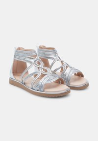 Zilveren sandalen met uitgebreide kruisingen van banden en lusdetails. Vlakke zolen, soepele binnenvoering en metallic accenten verbeteren het ontwerp.