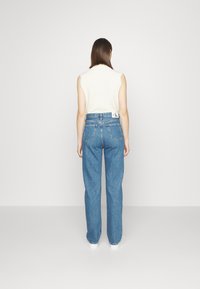 High-waisted blue denim jeans with a loose fit, featuring back pockets and a visible brand tag on the waistband.