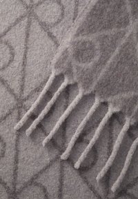 Couverture grise à motifs présentant des designs géométriques, texture douce et bords effilochés. Le matériau semble épais et douillet.