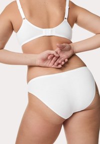 Soutien-gorge en coton blanc avec des bretelles réglables et une fermeture à crochet à l'arrière, associé à un slip en coton blanc assorti. Texture lisse, design minimaliste.