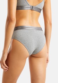 Donna vista da dietro che indossa biancheria intima e reggiseno grigi in cotone con elastici marchiati "United Colors of Benetton."