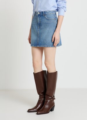 Minigonna di jeans azzurro chiaro, con vita aderente e orlo sfrangiato. Abbinate a stivali alti fino al ginocchio in pelle marrone con punta appuntita.