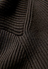 Strickstoff in Dunkelbraun mit vertikalem Rippenmuster und markanten Nahtdetails, die ein weiches, flexibles Erscheinungsbild vermitteln.