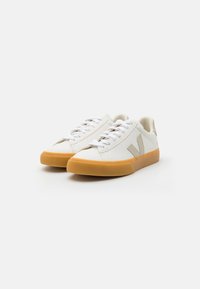 Hvite veganske lær sneakers med beige detaljer, rund tå og gummisåle i oransje. Har flate lisser og et teksturert side logo.