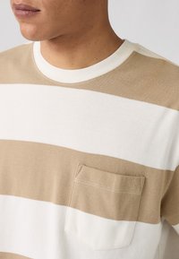 Beige and white striped sweater with a round neck, featuring a textured fabric and a small pocket on the left chest.