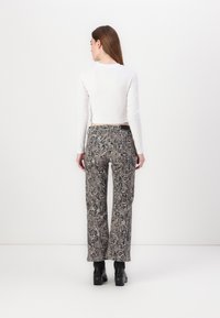 Pantalons évasés avec un motif serpent noir et beige, dotés d'une taille haute et de détails texturés subtils. Associés à un haut blanc.