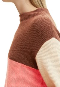 Sweter dziergany z wysokim kołnierzem, w kolorach brązowym, różowym i kremowym. Tekstura wykonana w prążki, tworząca unikalny wzór wizualny.