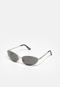 Lunettes de soleil avec une monture en métal argenté �élégant, des verres teintés gris et un design aérodynamique avec des bords pointus et des branches fines.